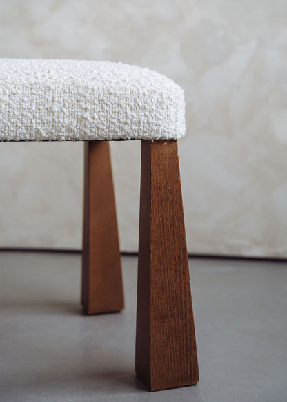 Silla de madera de haya tapizada en bouclé blanco con respaldo triangular.