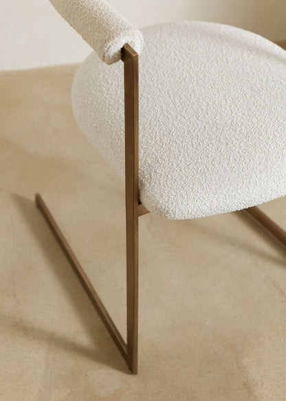 Silla de latón con acabado cepillado, tapizada con bouclé blanco.