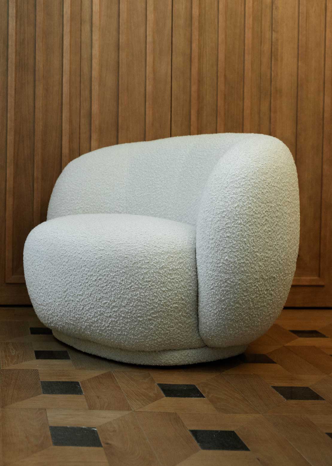 Sillón tapizado con tela bouclé blanca.
