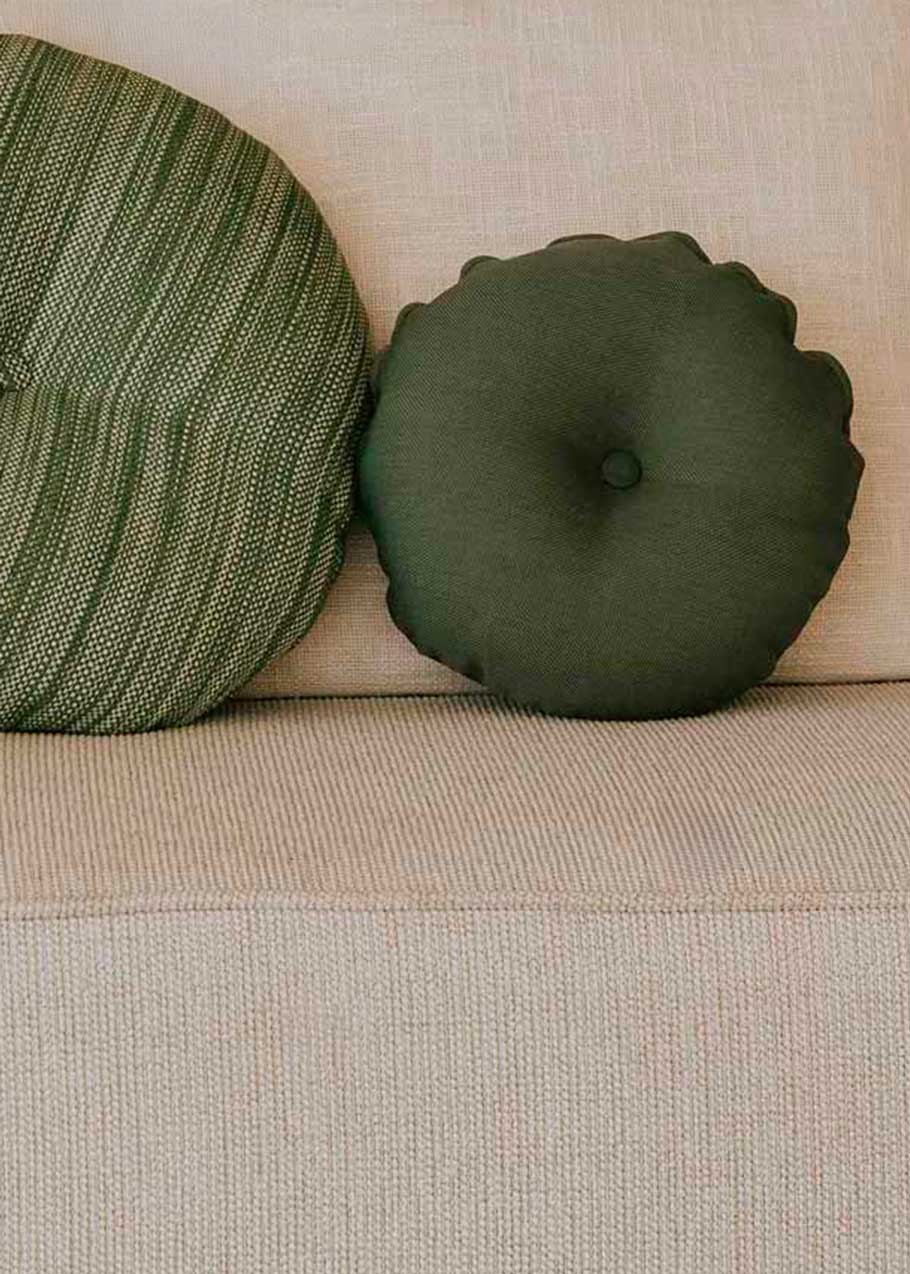 Almohadón circular con capitoné, tapizado en tela verde.