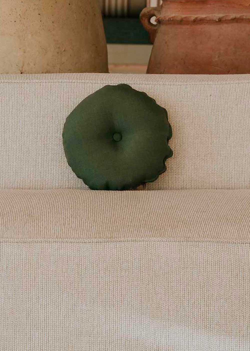 Almohadón circular con capitoné, tapizado en tela verde.