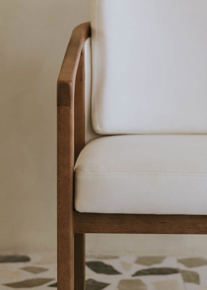 Butaca de exterior en madera de haya con reposabrazos tapizada en tela blanca.