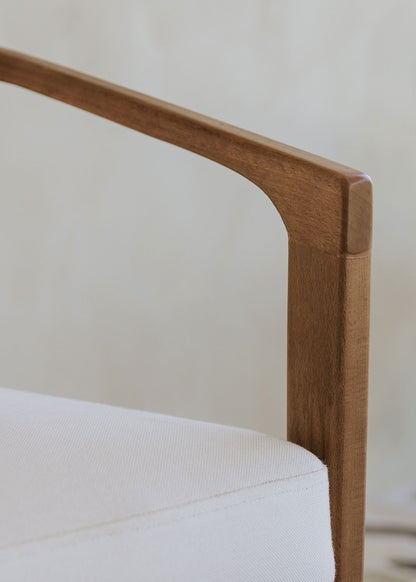 Butaca de exterior en madera de haya con reposabrazos tapizada en tela blanca.