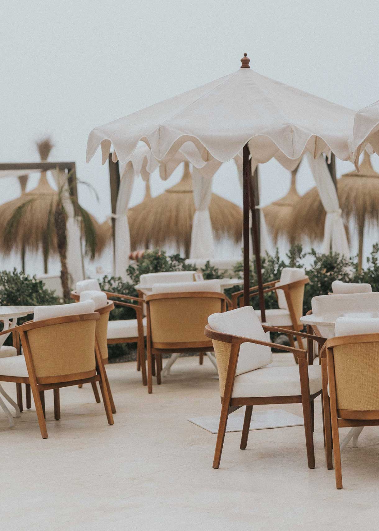 Butaca de exterior en madera de haya con reposabrazos tapizada en tela blanca.