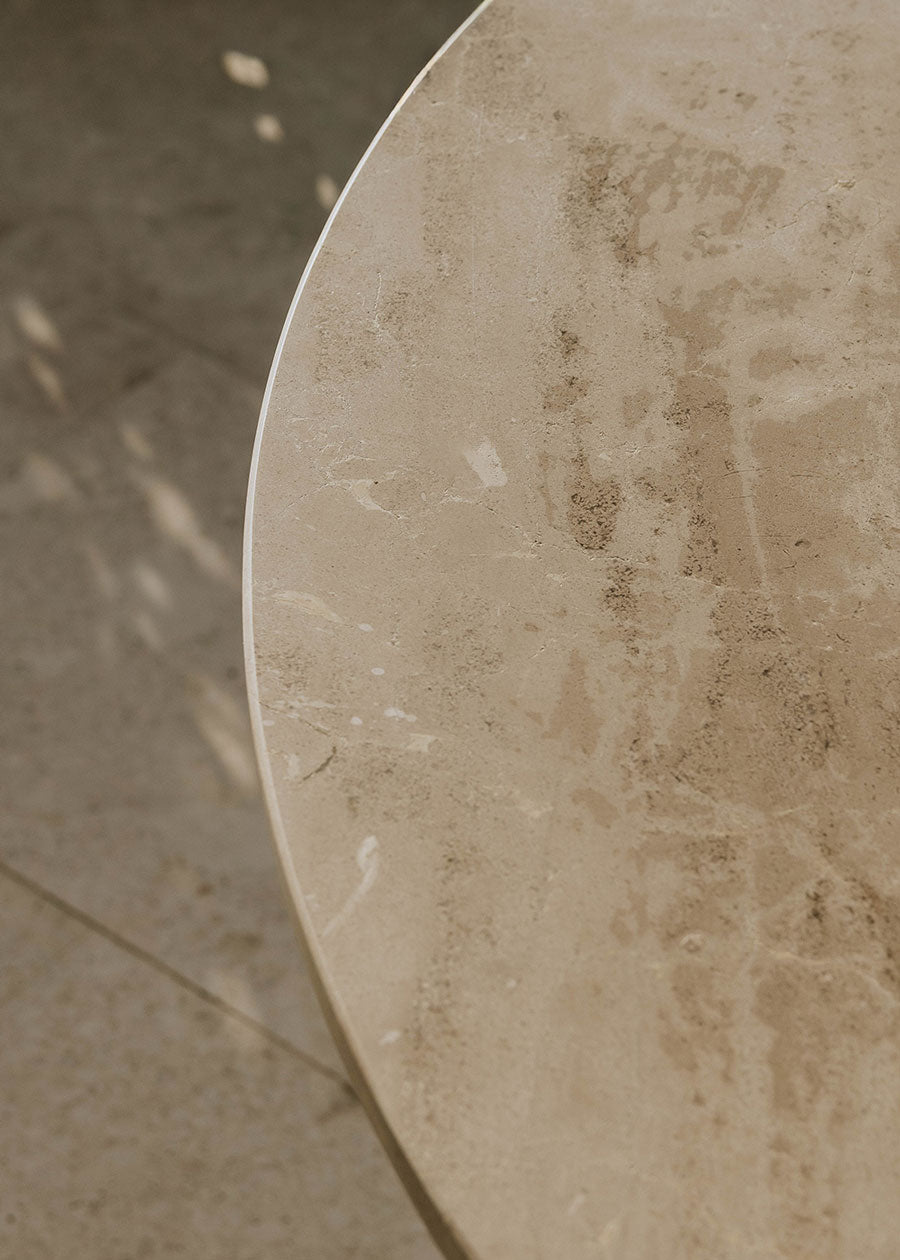 Mesa de exterior circular con estructura de hierro forjado acabado en blanco y sobre de mármol crema marfil.