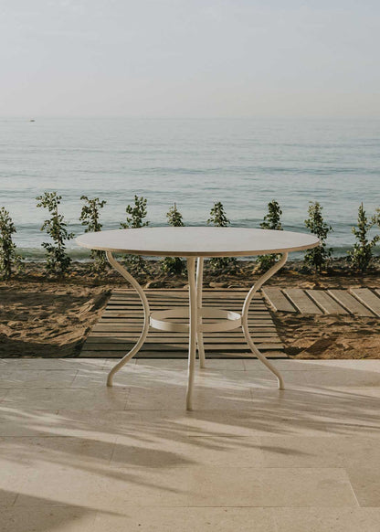 Mesa de exterior circular con estructura de hierro forjado acabado en blanco y sobre de mármol crema marfil.