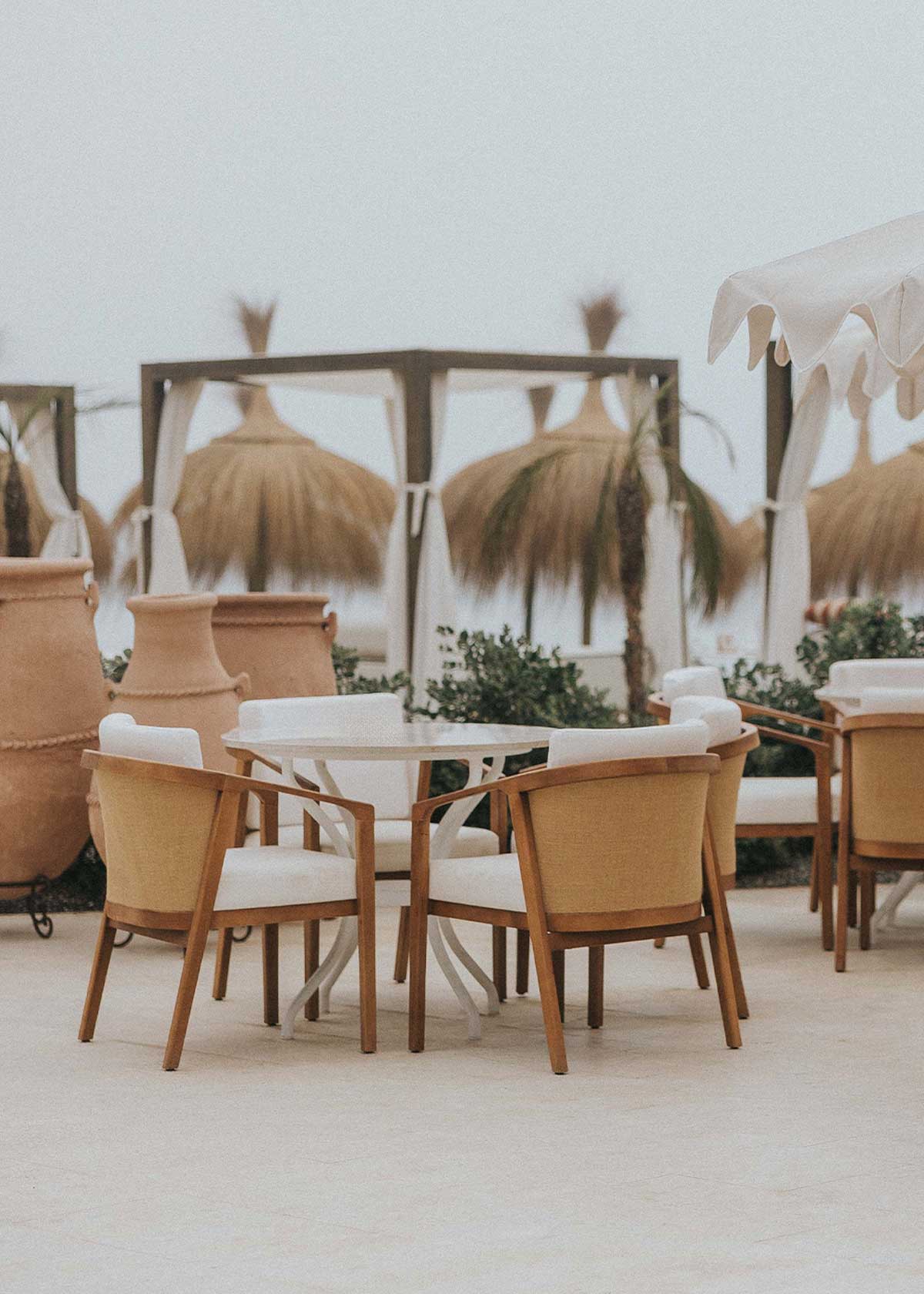 Mesa de exterior circular con estructura de hierro forjado acabado en blanco y sobre de mármol crema marfil.