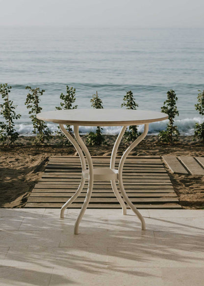 Mesa de exterior circular con estructura de hierro forjado acabado en blanco y sobre de mármol crema marfil.