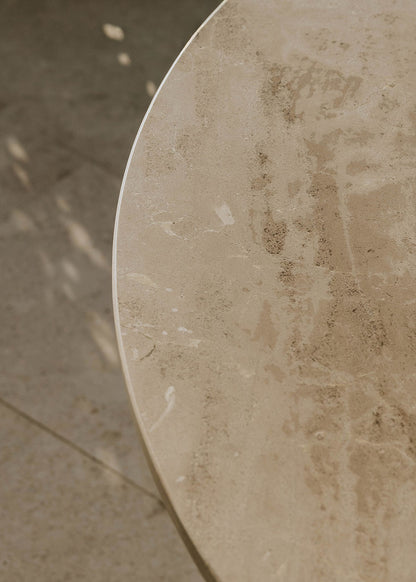 Mesa de exterior circular con estructura de hierro forjado acabado en blanco y sobre de mármol crema marfil.