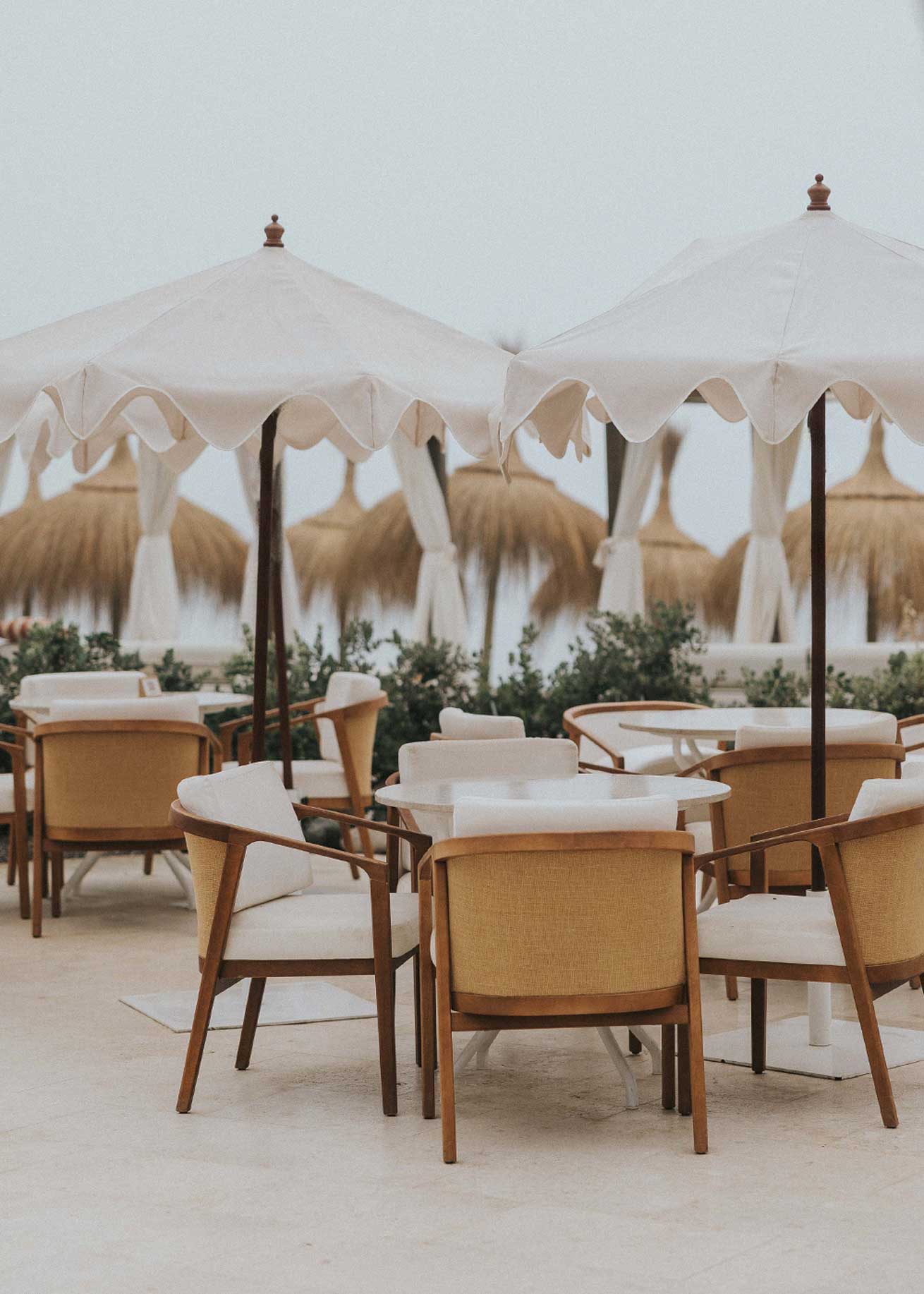 Mesa de exterior circular con estructura de hierro forjado acabado en blanco y sobre de mármol crema marfil.