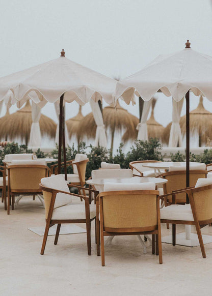 Mesa de exterior circular con estructura de hierro forjado acabado en blanco y sobre de mármol crema marfil.