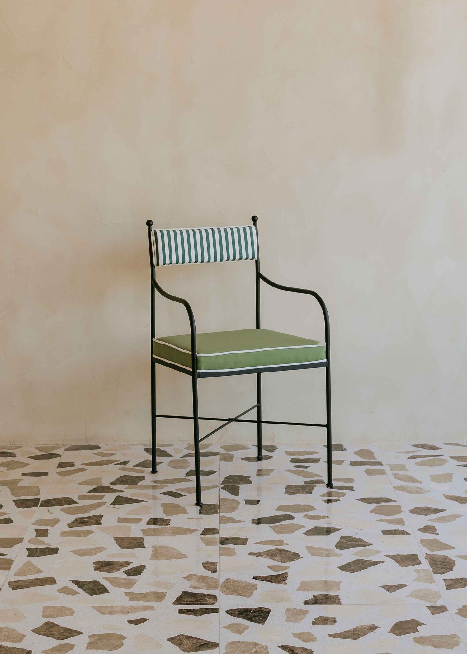 Silla de exterior con estructura de hierro negro tapizada en verde y blanco.