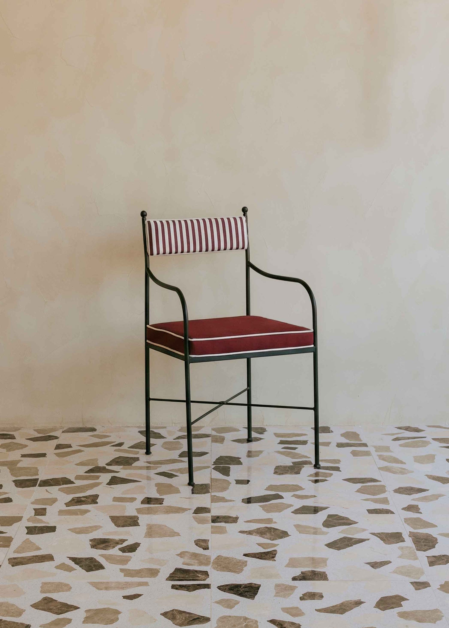 Silla de exterior con estructura de hierro negro tapizada en granate y blanco.