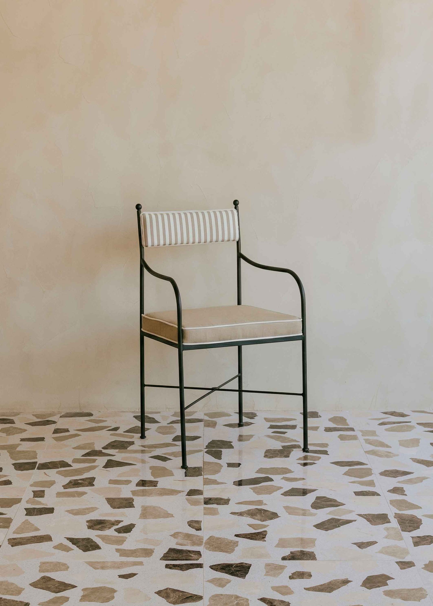 Silla de exterior con estructura de hierro negro tapizada en beige y blanco.