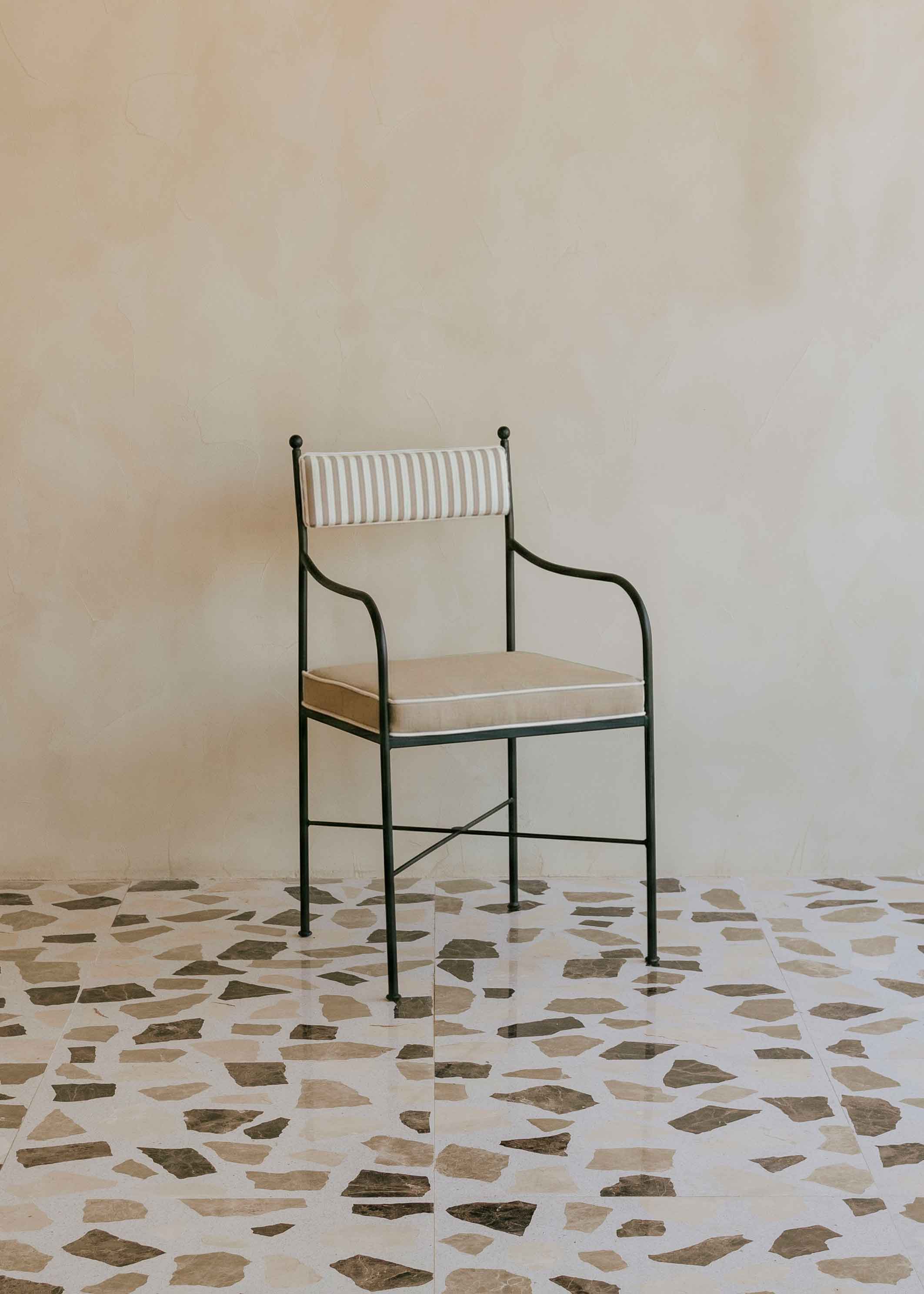 Silla de exterior con estructura de hierro negro tapizada en beige y blanco.