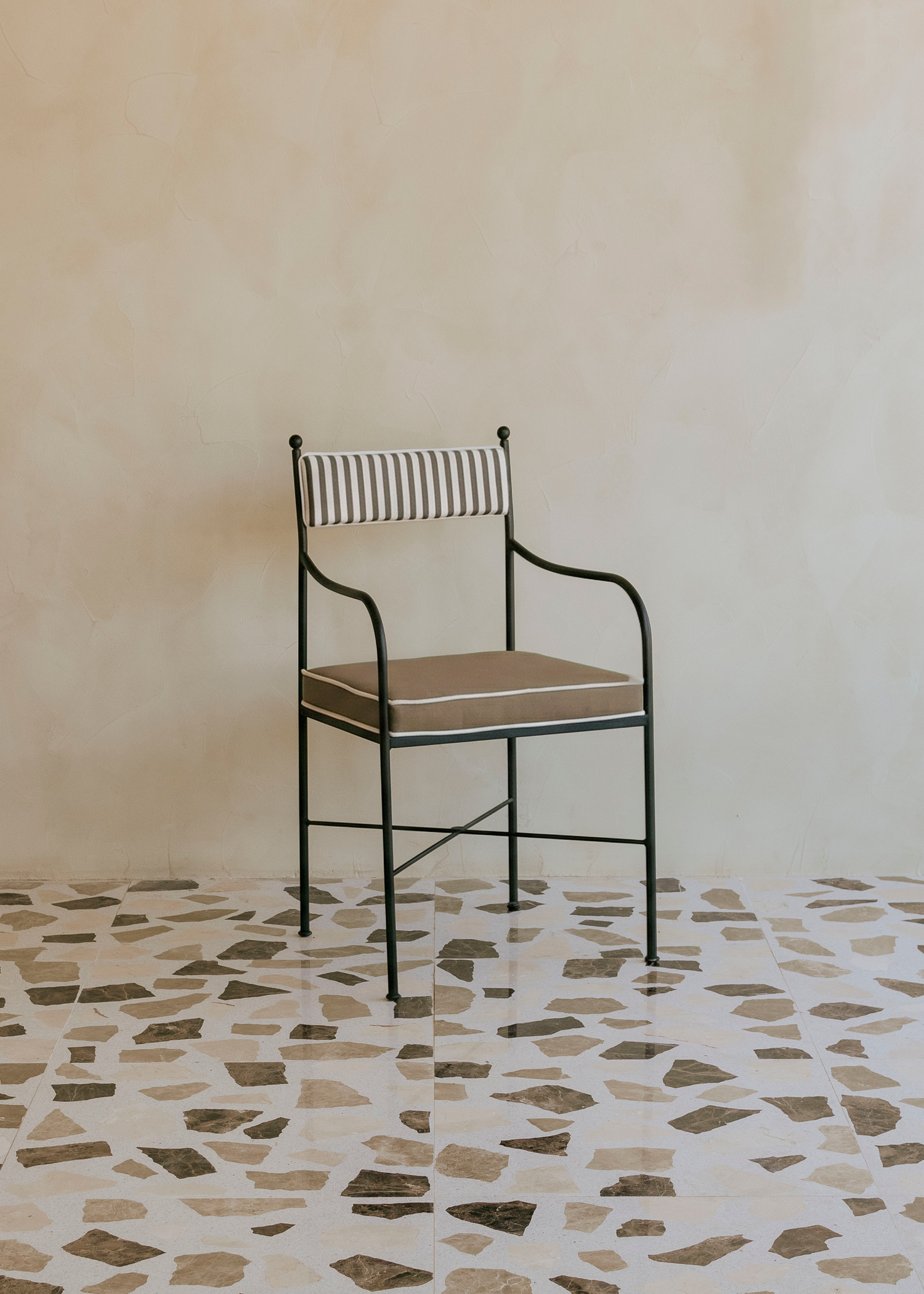 Silla de exterior con estructura de hierro negro tapizada en color topo y blanco.