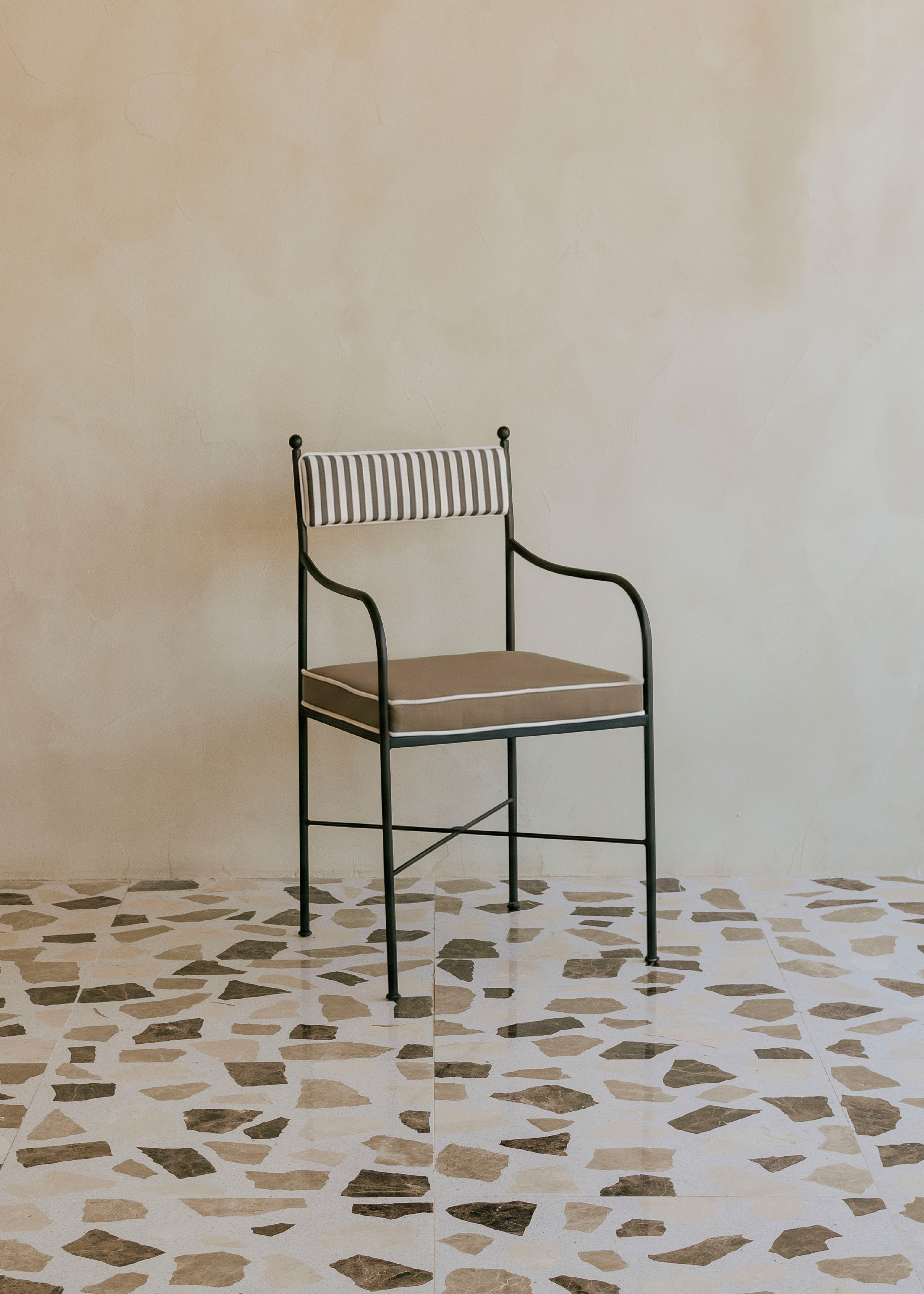 Silla de exterior con estructura de hierro negro tapizada en color topo y blanco.