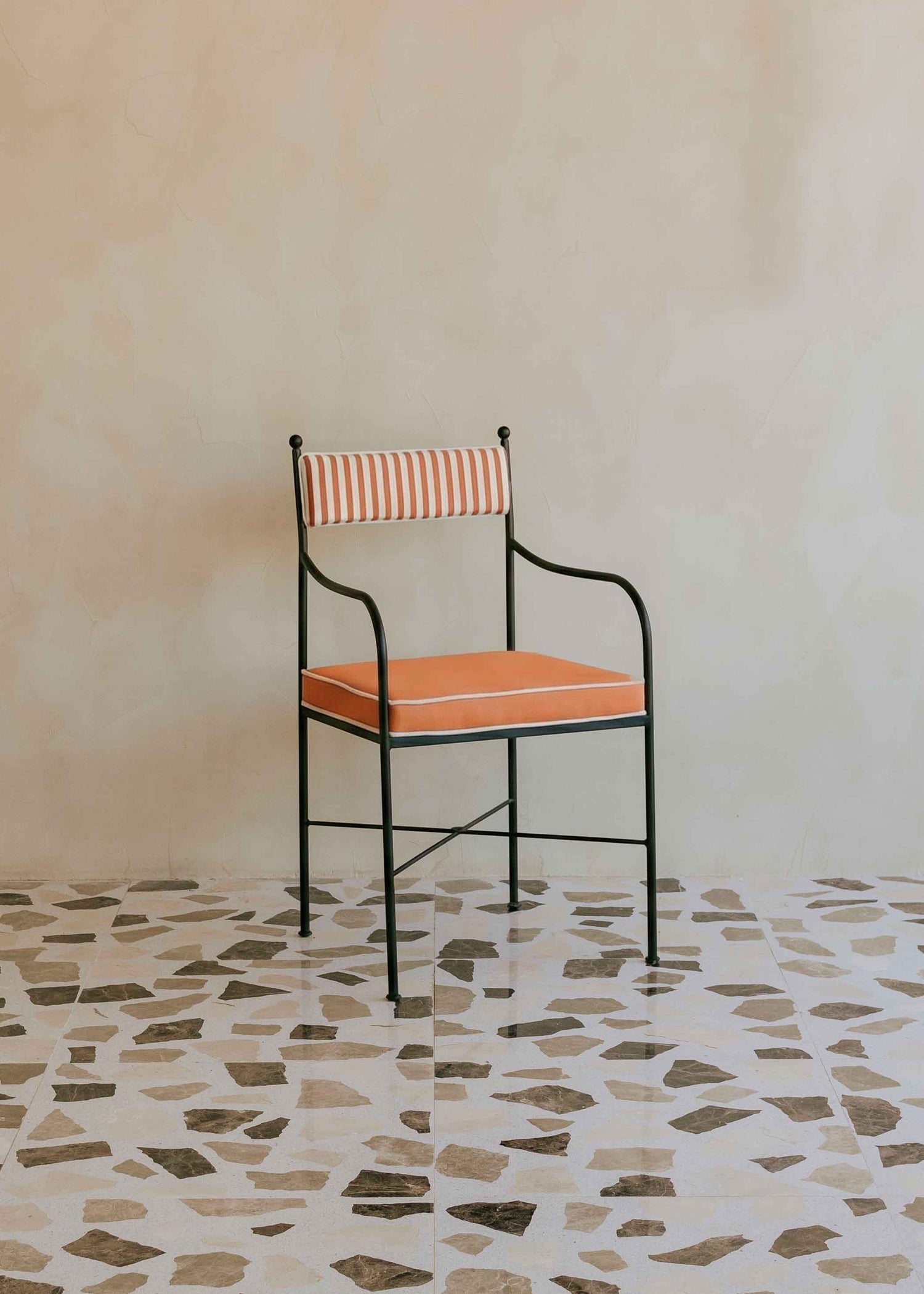Silla de exterior con estructura de hierro negro tapizada en naranja y blanco.