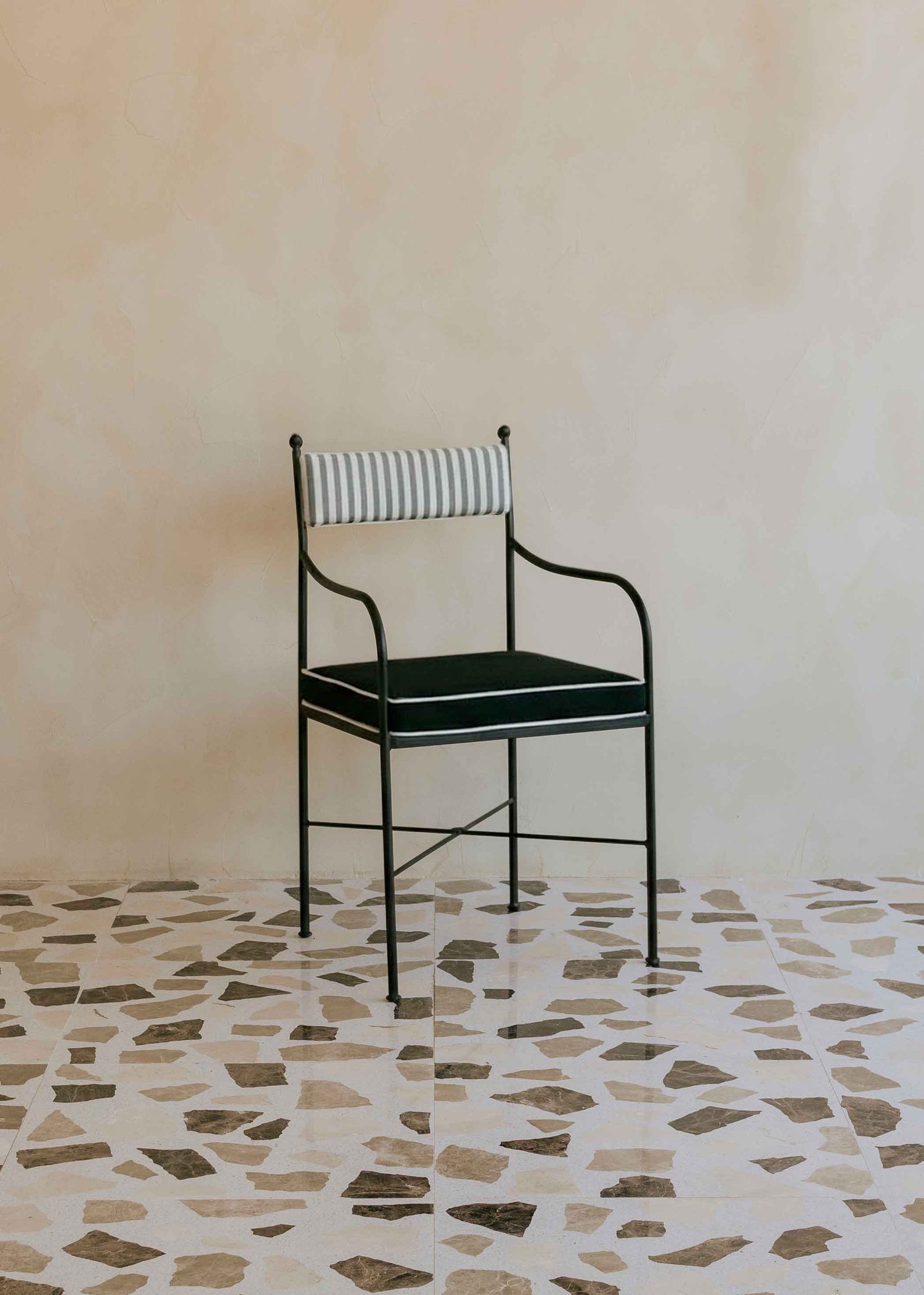 Silla de exterior con estructura de hierro negro tapizada en gris, negro y blanco.