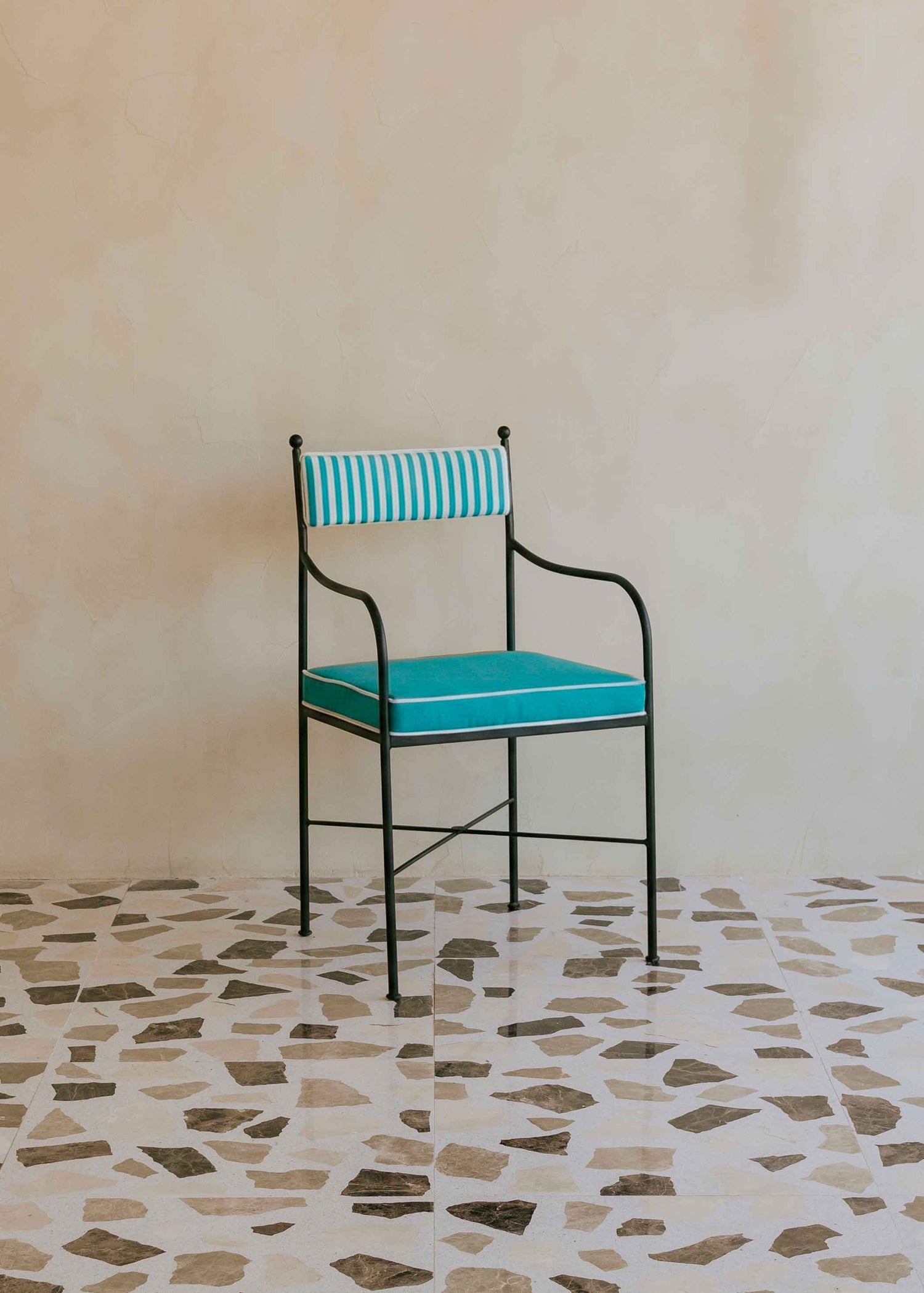 Silla de exterior con estructura de hierro negro tapizada en azul turquesa y blanco.