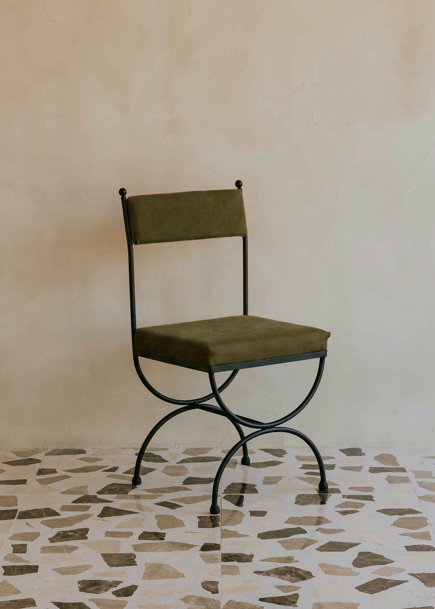 Silla de exterior con estructura de hierro negro tapizada en color verde musgo.