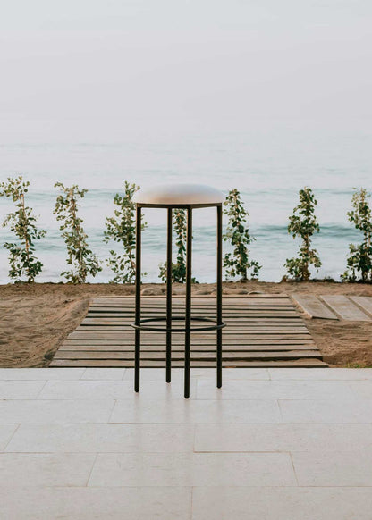 Taburete con estructura de hierro acabado en negro tapizado en tela blanca.