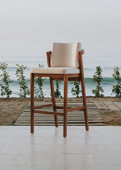 Taburete de exterior en madera de haya con respaldo tapizado en tela blanca.