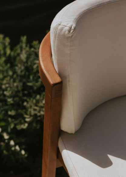 Taburete de exterior en madera de haya con respaldo tapizado en tela blanca.