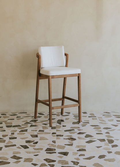 Taburete de exterior en madera de haya con respaldo tapizado en tela blanca.