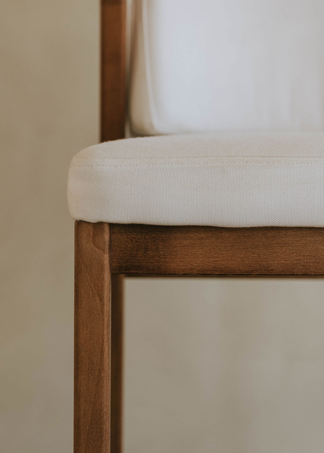 Taburete de exterior en madera de haya con respaldo tapizado en tela blanca.