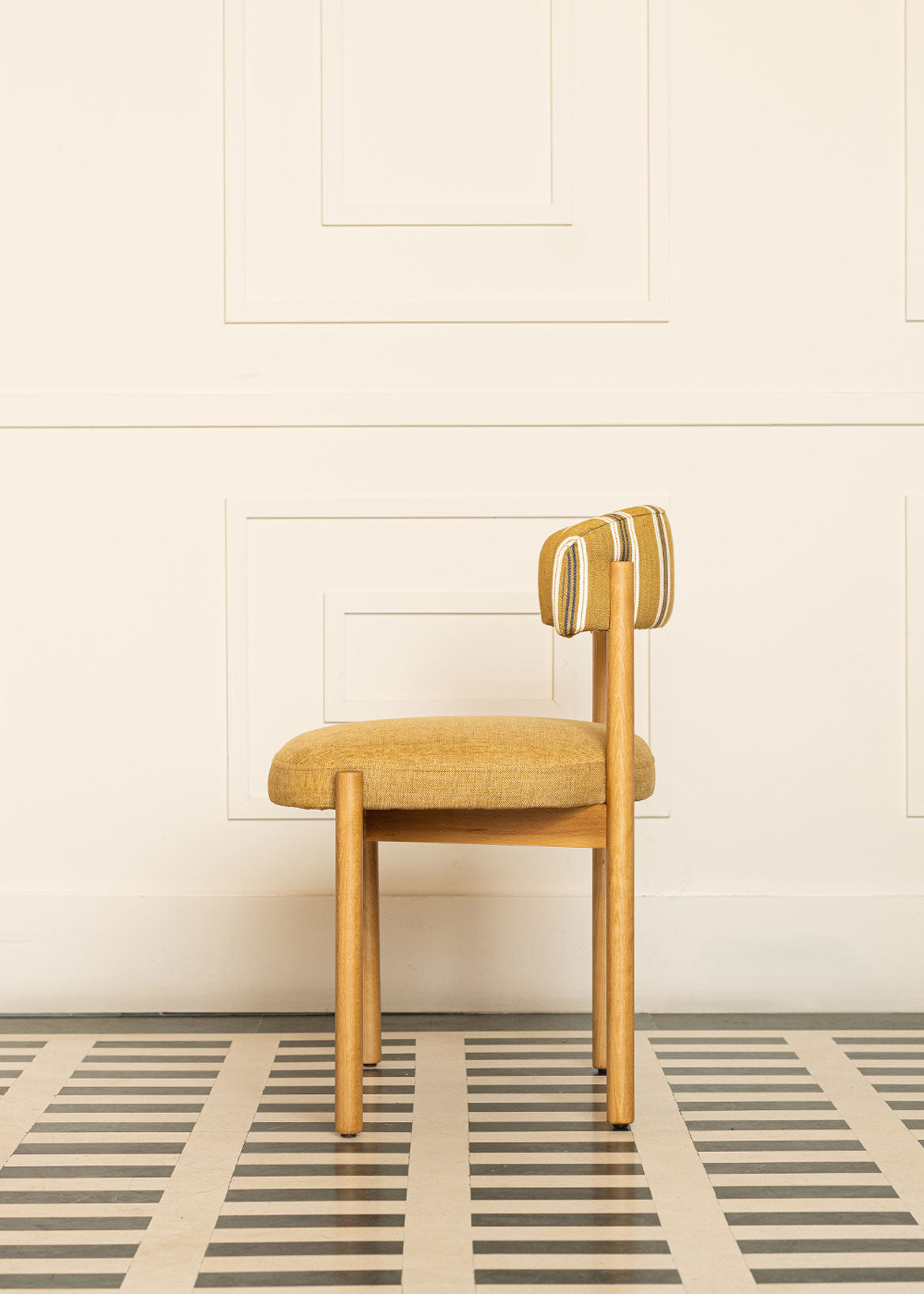 Silla de madera de haya con asiento tapizado en tela mostaza y respaldo con estampado de rayas.