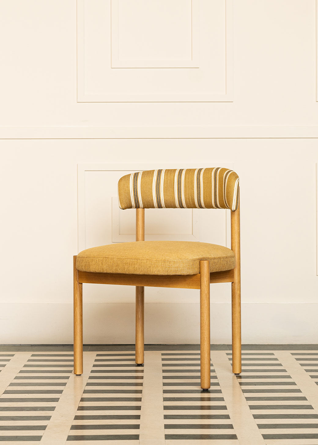 Silla de madera de haya con asiento tapizado en tela mostaza y respaldo con estampado de rayas.