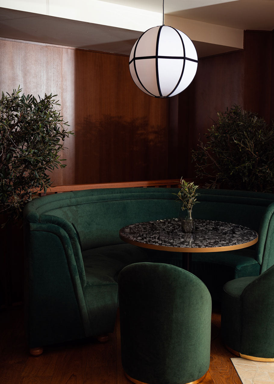 Banco curvado tapizado en terciopelo verde con patas de madera de haya.