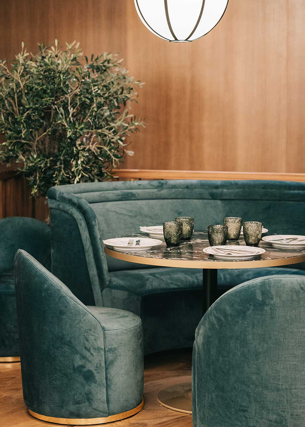 Banco curvado tapizado en terciopelo verde con patas de madera de haya.