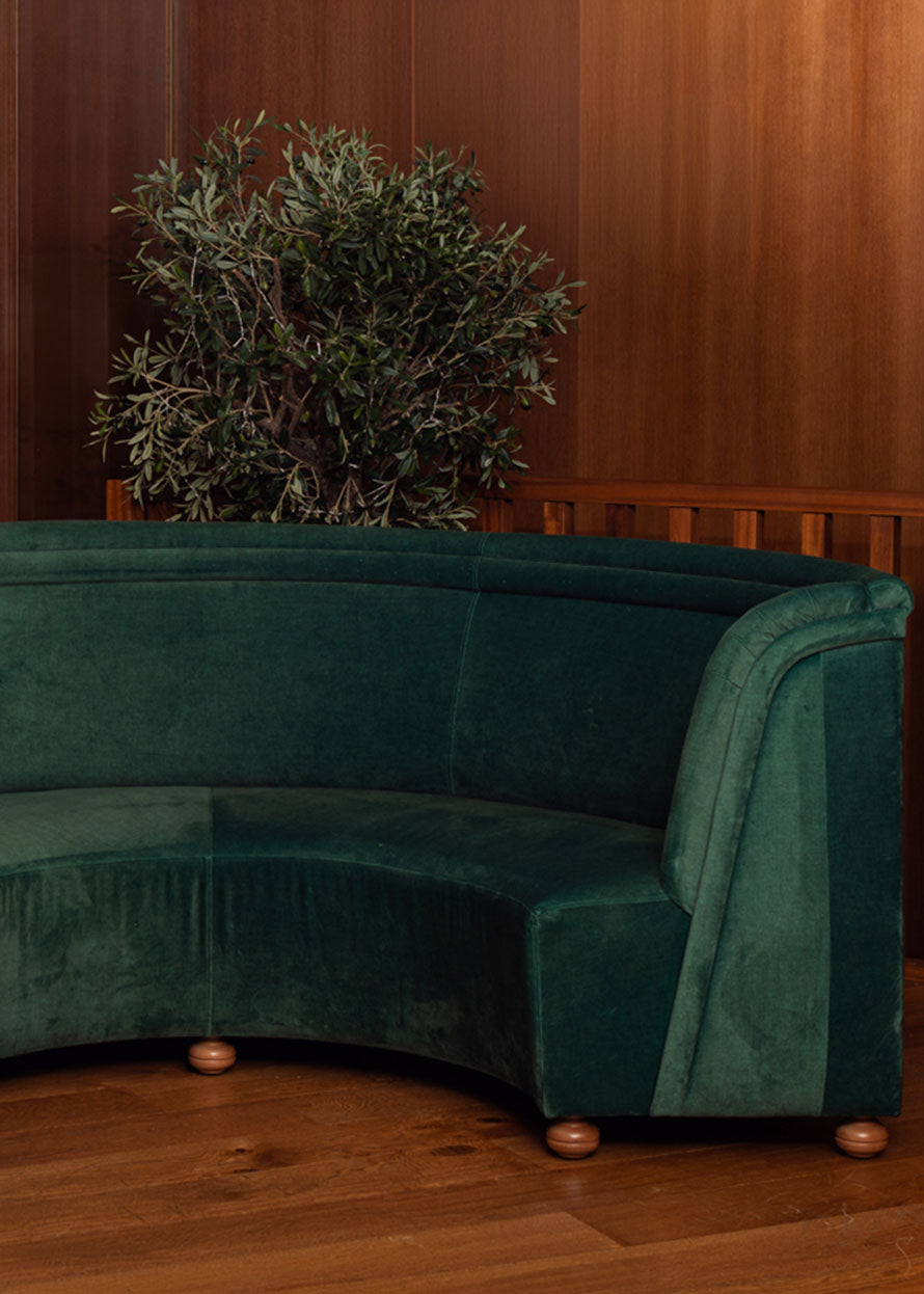 Banco curvado tapizado en terciopelo verde con patas de madera de haya.