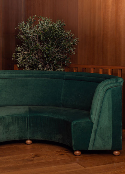 Banco curvado tapizado en terciopelo verde con patas de madera de haya.