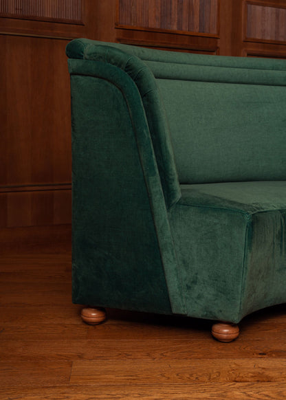 Banco curvado tapizado en terciopelo verde con patas de madera de haya.