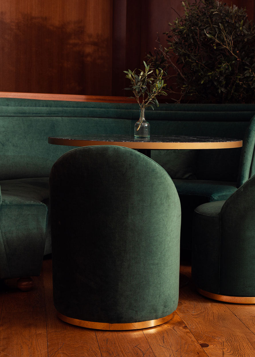 Butaca tapizada en terciopelo verde con zócalo dorado en la base.