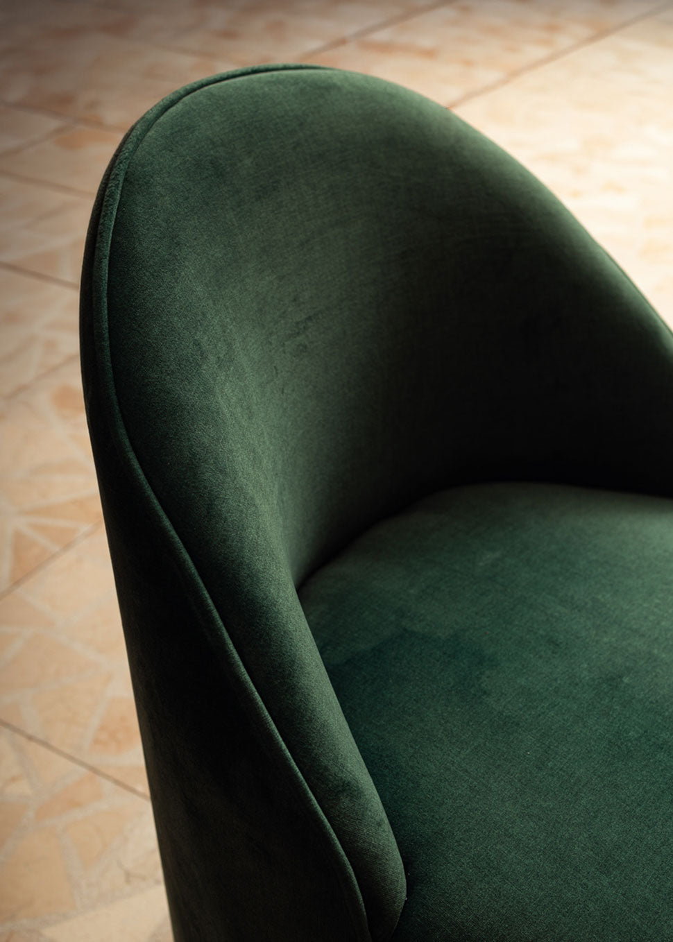 Butaca tapizada en terciopelo verde con zócalo dorado en la base.