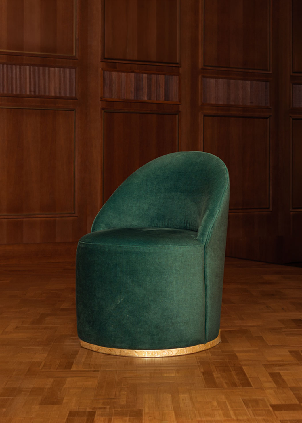 Butaca tapizada en terciopelo verde con zócalo dorado en la base.