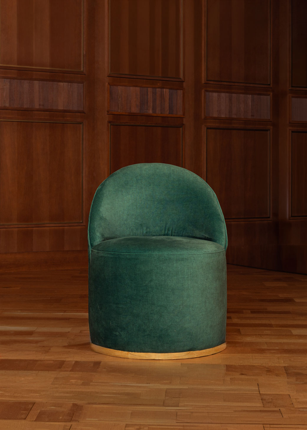 Butaca tapizada en terciopelo verde con zócalo dorado en la base.
