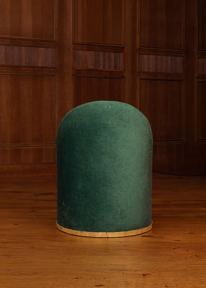 Butaca tapizada en terciopelo verde con zócalo dorado en la base.
