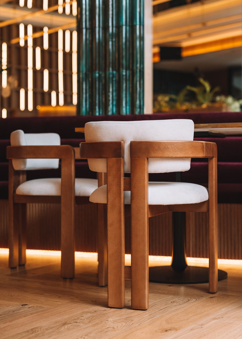 Silla de madera de haya con reposabrazos tapizada en terciopelo beige.