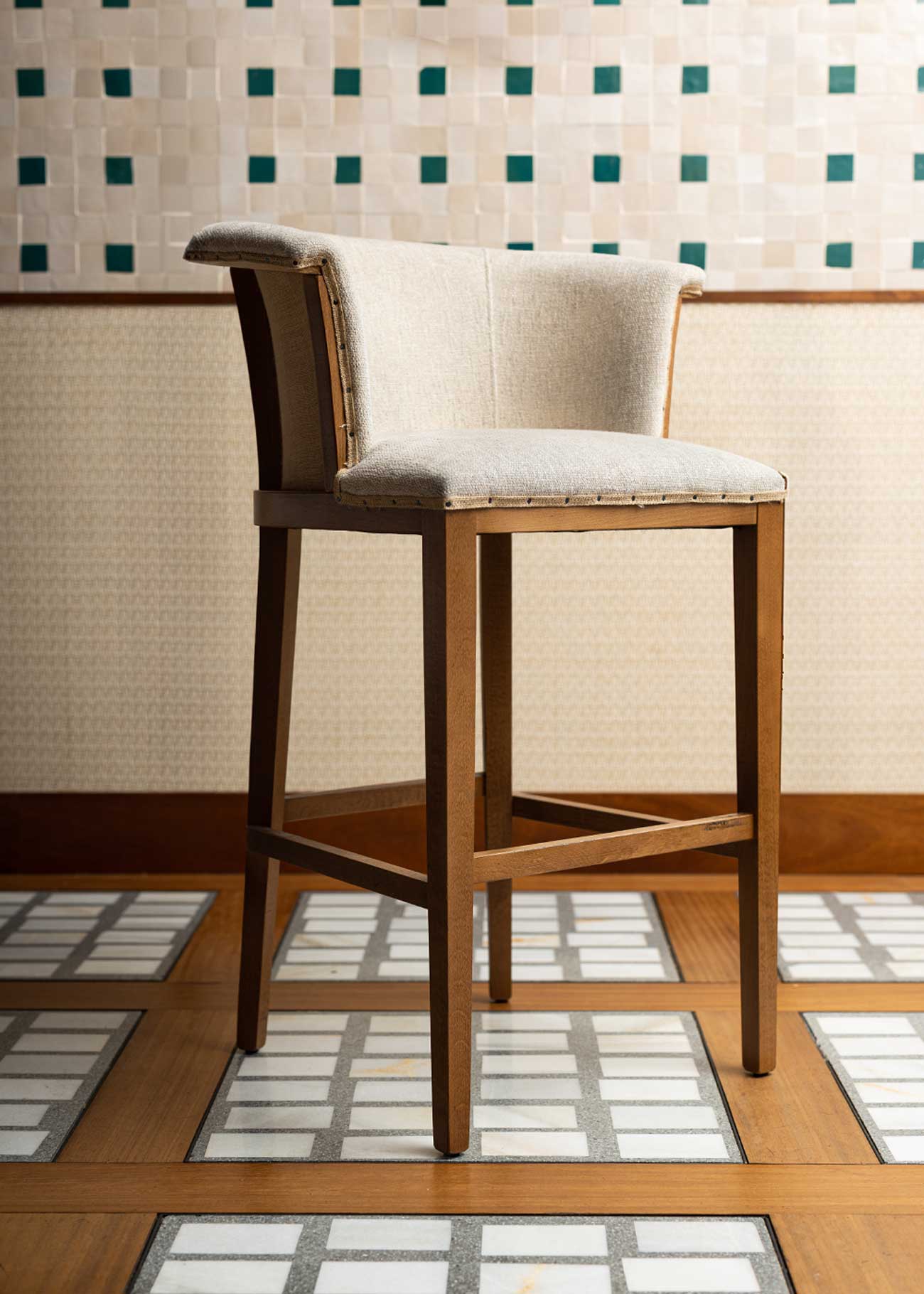 Taburete con estructura de madera de haya, tapizado en tela beige y acabado con un ribete de yute con remaches.