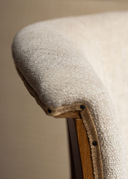 Taburete con estructura de madera de haya, tapizado en tela beige y acabado con un ribete de yute con remaches.