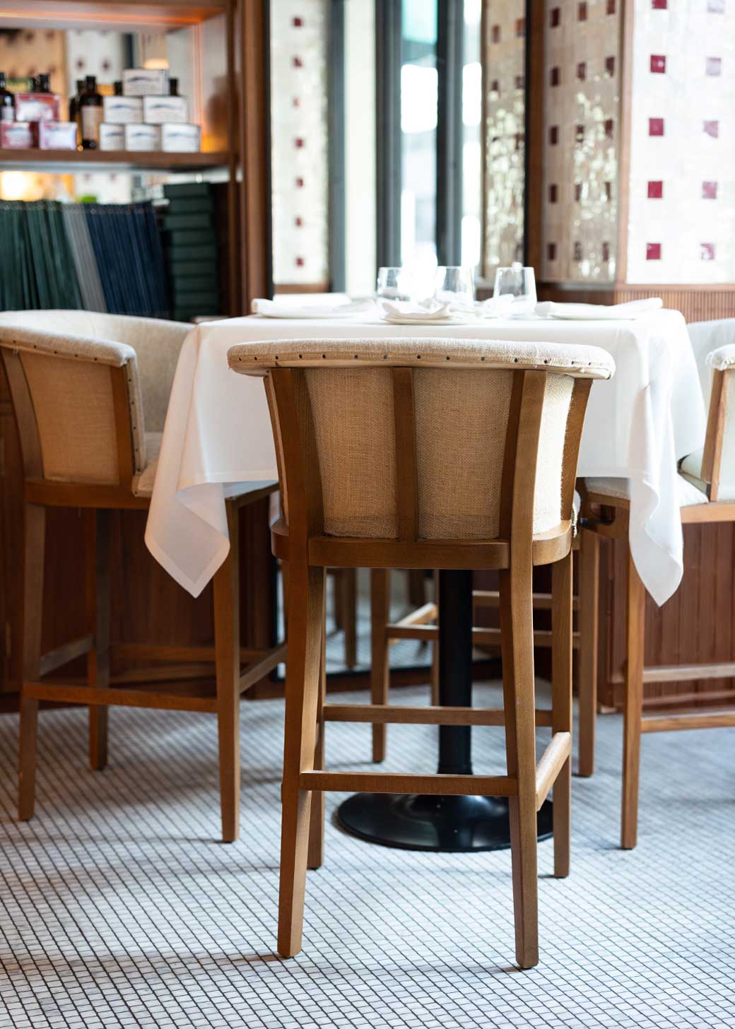 Taburete con estructura de madera de haya, tapizado en tela beige y acabado con un ribete de yute con remaches.