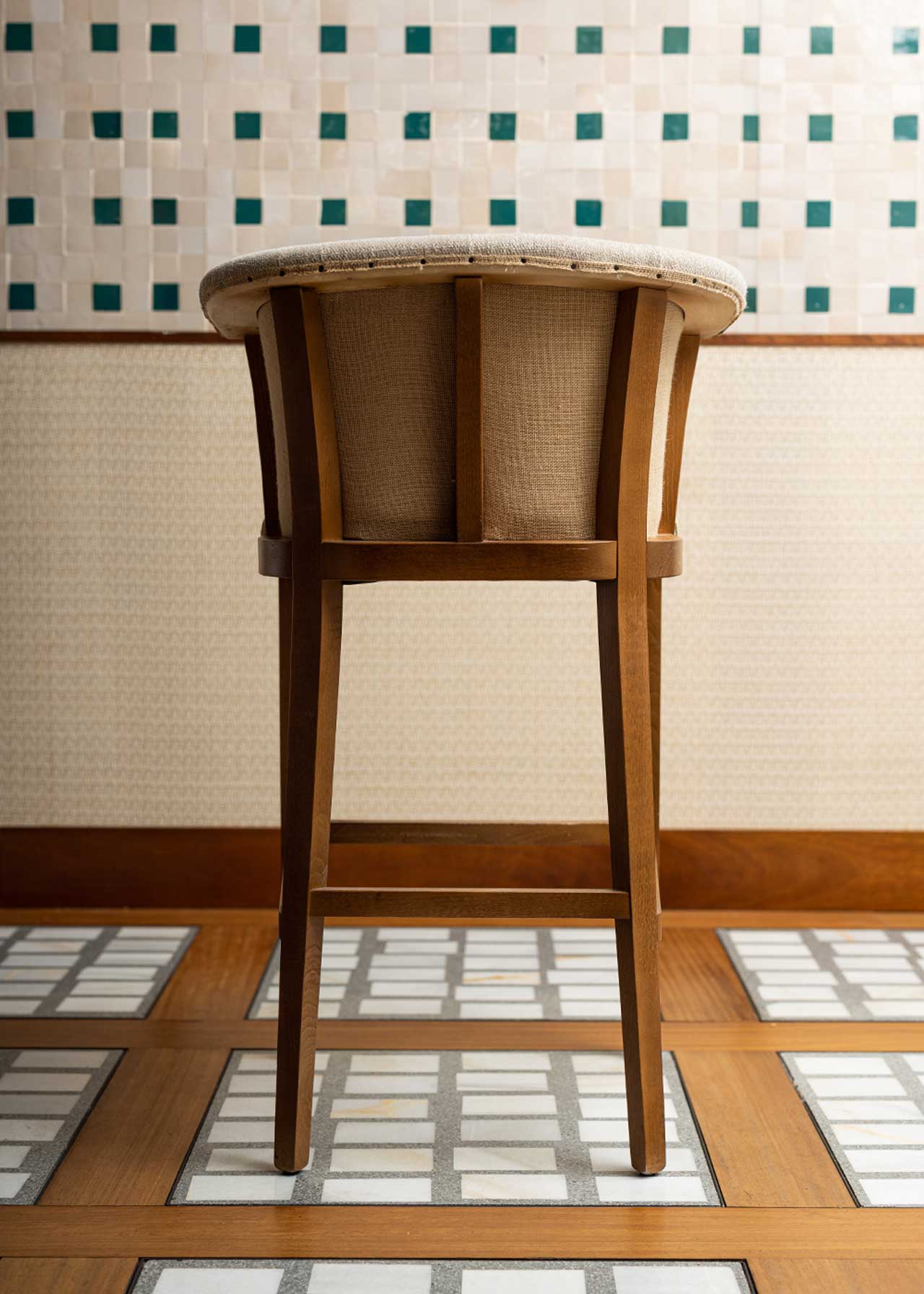 Taburete con estructura de madera de haya, tapizado en tela beige y acabado con un ribete de yute con remaches.