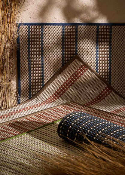 Alfombra fabricada en PET a partir de botellas de plástico recicladas de color beige con detalles en teja y elaborada en telar wilton de tejido plano.