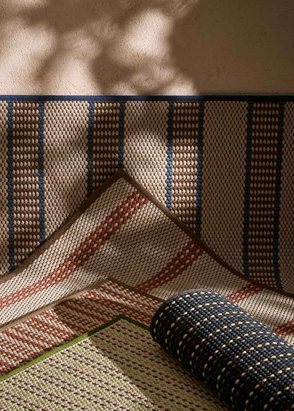 Alfombra fabricada en PET a partir de botellas de plástico recicladas de color beige con detalles en teja y elaborada en telar wilton de tejido plano.